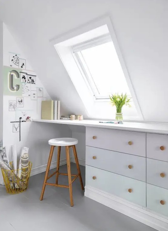 A Nordic attic home office in white, with a skylight, a built in desk, a stool and a small gallery wall plus blooms