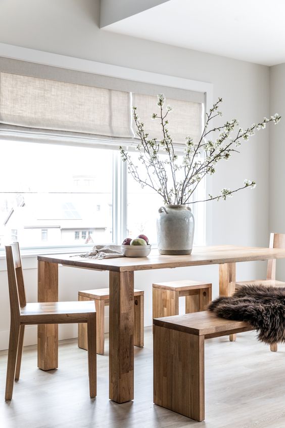 a Nordic dining room with a wooden dining table, chairs, benches, neutral shades and a grey vase with blooming branches