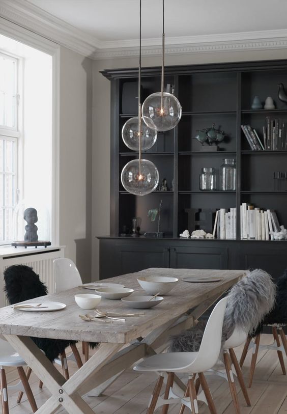 a Nordic dining space with a black storage unit, a reclaimed trestle dining table, matching white chairs and pendant lamps