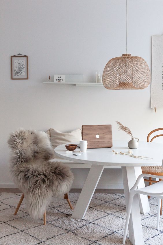 a Nordic dining space with a white round table, a bench, mismathing chairs, a woven pendant lamp