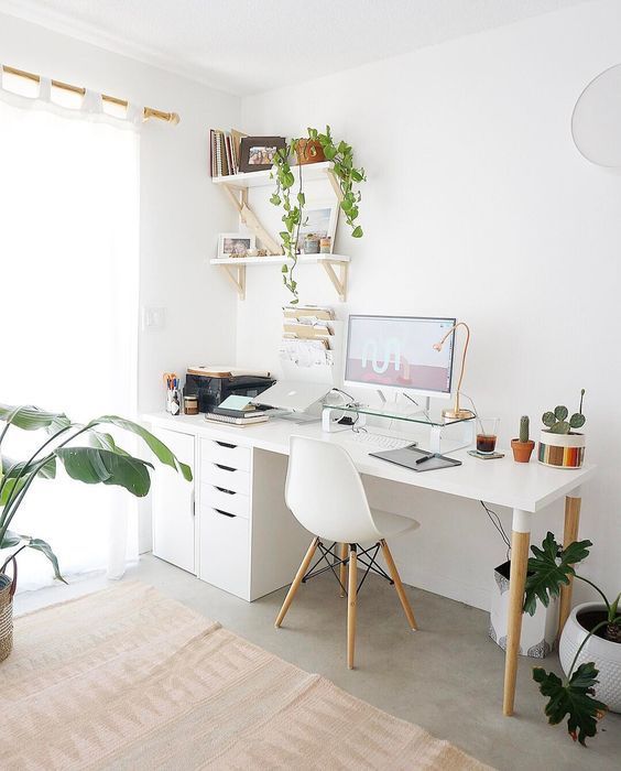A Nordic home office with a white desk, file cabinets, a white chair, wall mounted shelves, potted plants and touches of gold