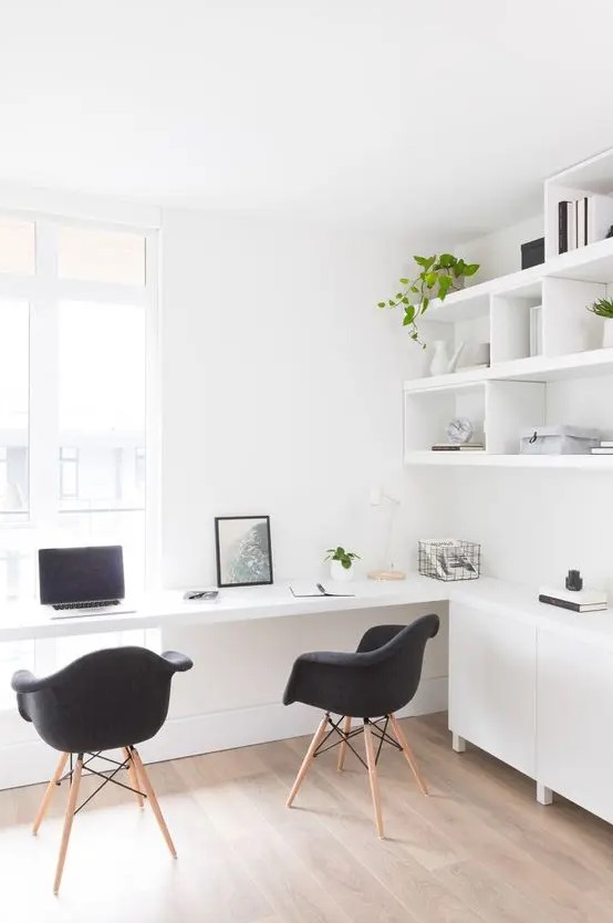 A Nordic light filled working space with open shelves and sleek cabinets, a built in desk and black chairs and potted greenery