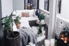 a Scandinavian balcony with a wicker corner sofa with white upholstery, candles and potted plants, some blooms and pendant lamps