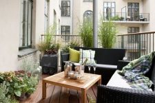 a Scandinavian balcony with black wicker furniture, a stained table, potted plants and blooms and printed textiles
