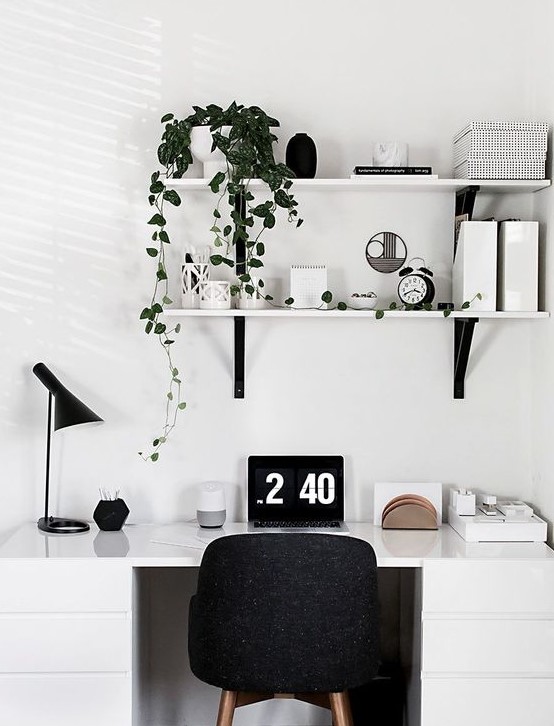 A Scandinavian home office nook with a white desk, a black chair, lamp and some wall mounted shelves