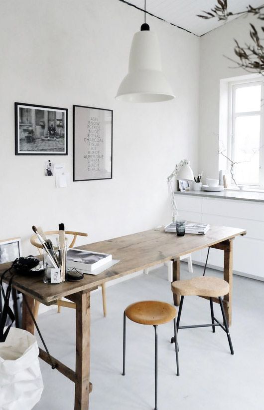A Scandinavian home office with a wooden desk, cork stools and a wooden chair, a pendant lamp, artworks and a built in storage unit
