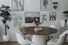 a catchy Scandinavian dining space with a round table, white chairs, a black and white gallery wall and potted plants