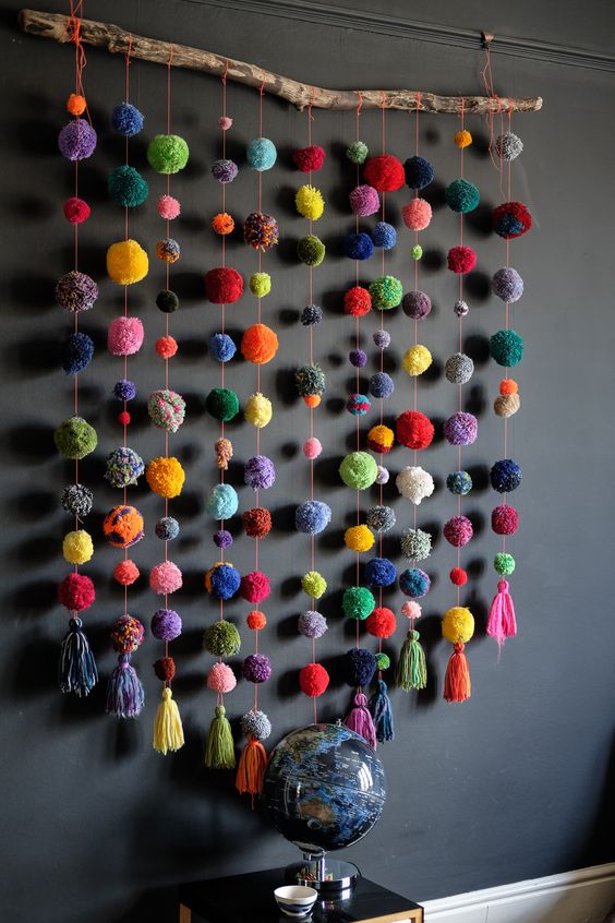 a colorful stick and pompom wall hanging is a bright and fun decoration that can be made in minutes