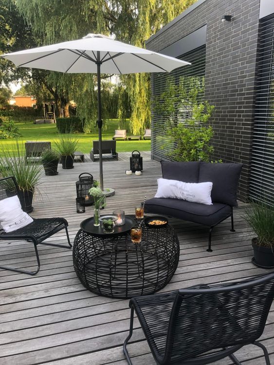 a contrasting Scandinavian terrace with black seating furniture, a black coffee table, a white umbrella and potted greenery