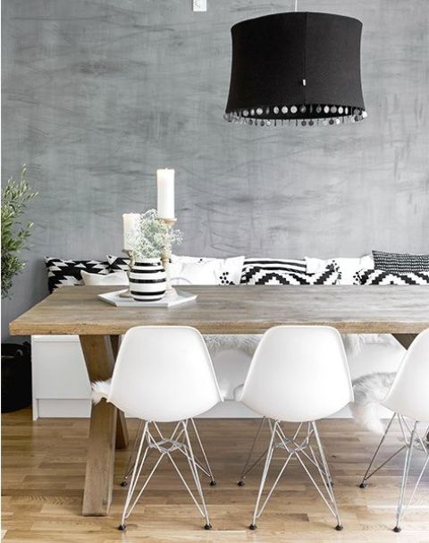 a cool Scandinavian dining space with a white storage bench with black and white pillows, a stained trestle table, white matching chairs and a black pendant lamp