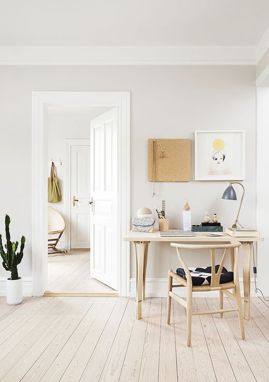 a cozy neutral Nordic home office with some wooden furniture, art on the wall and a cactus in a pot