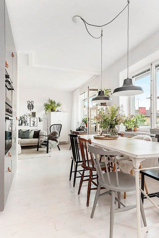 a cute Scandinavian dining space wiht a white vintage dining table, mismacthing vintage chairs, black pendant lamps and greenery