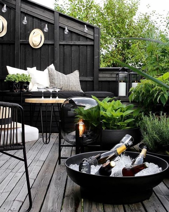 a dark Nordic terrace with blakc walls, planters and bowls, metal and wooden furniture, a catchy floor lamp and greenery that refreshes the space