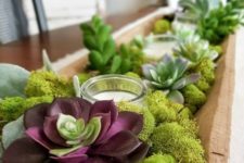 a dough bowl centerpiece with moss, succulents and candles in a glass candle holder is a trendy idea