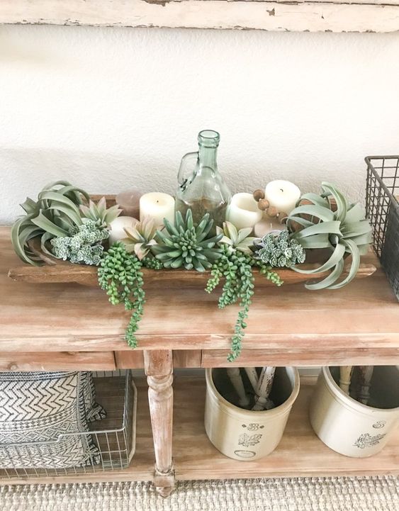 a dough bowl decoration with succulents, air plants, pillar candles and a vintage bottle