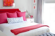 a dove grey bedroom with a bold red upholstered bed, pink and neutral pillows, a bold red blanket, a grey chair, a crystal chandelier