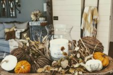 a fall decoration of a weathered dough bowl, fake pumpkins of various materials, dried leaves and a pillar candle