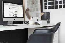 a laconic Nordic home office with a black statement wall and chair, a black noteboard, a white desk and a relaxed artwork
