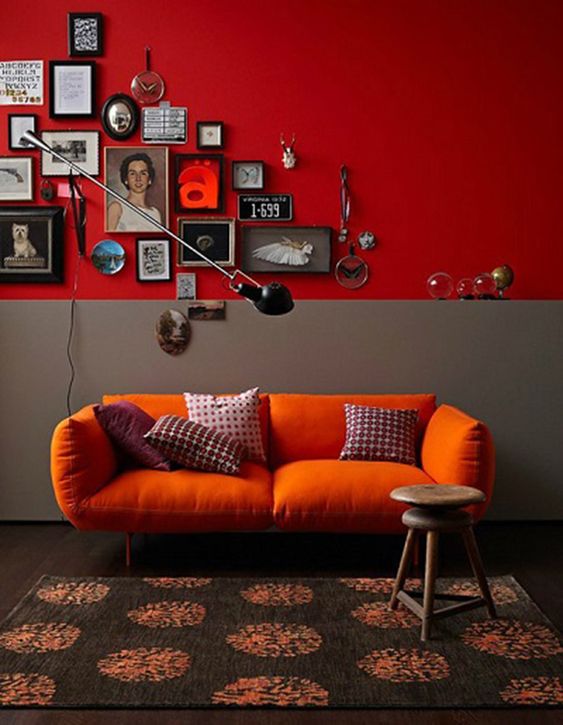 a lovely nook with a deep red and grey accent wall, an orange sofa, printed pillows, a catchy gallery wall and a wall sconce