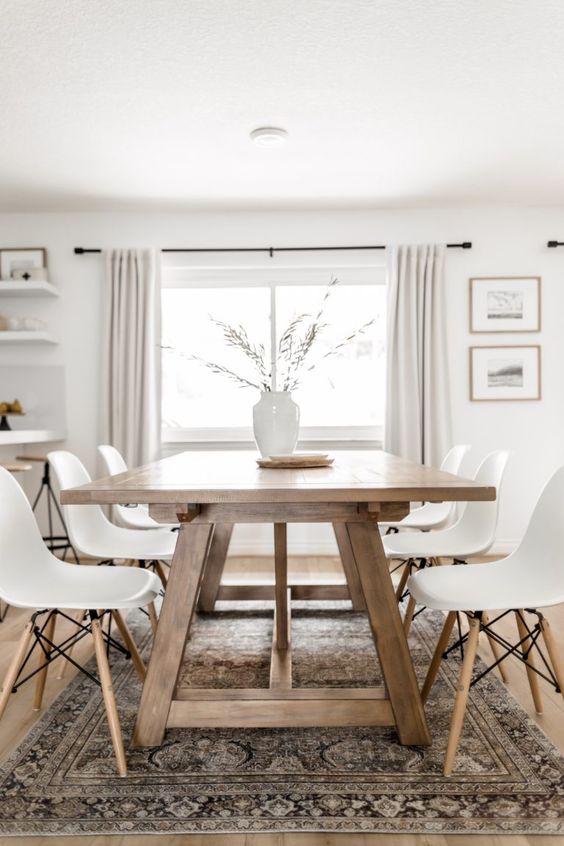 a modern Scandi dining room with a stained trestle dining table, white chairs, a printed rug, a vase with greenery