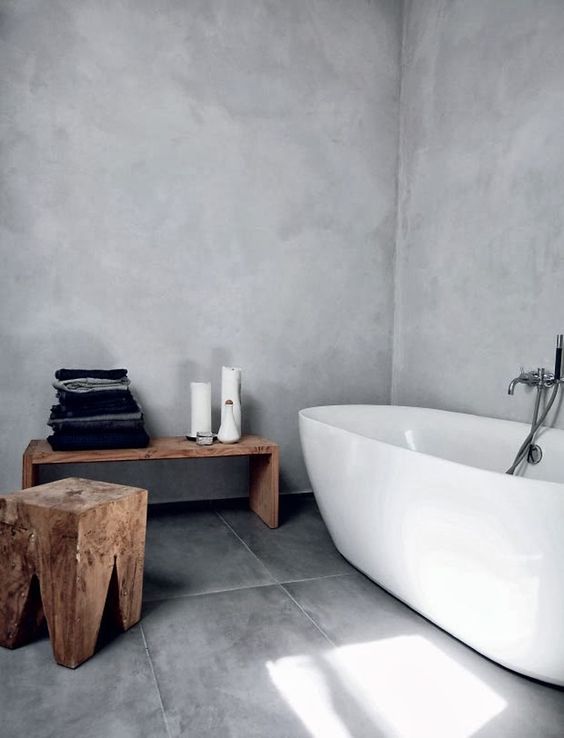 a natural Scandinavian bathroom done with concrete and grey tiles plus wooden stools and a bench