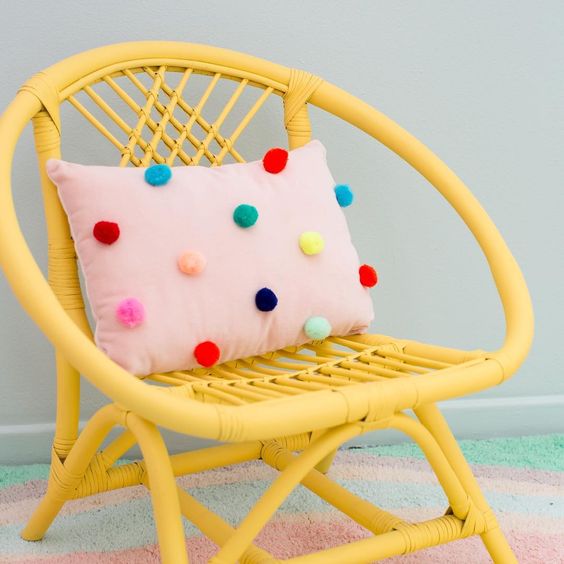 a pink pillow with colorufl pompoms accenting it is a cheerful and bright accessory that you can easily DIY