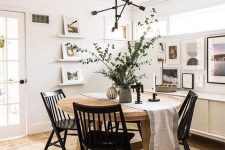 a pretty modern Nordic dining room with a round stained table, black chairs, a chandelier, a gallery wall and ledges with art