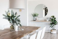 a refined Scandinavian dining room with a sleek table, white woven chairs, a tan pendant lamp and potted plants