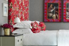 a refined bedroom with grey walls, a tall grey upholstered bed with a bold red floral headboard and pillows, bright artwork and a vintage dresser