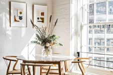 a round table with a bright tabletop, woven chairs, a muted color mini gallery wall and a floral arrangement with greenery