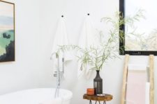 a serene Scandinavian bathroom with an oval tub, a wooden stool with hairpin legs and a blakc frame window