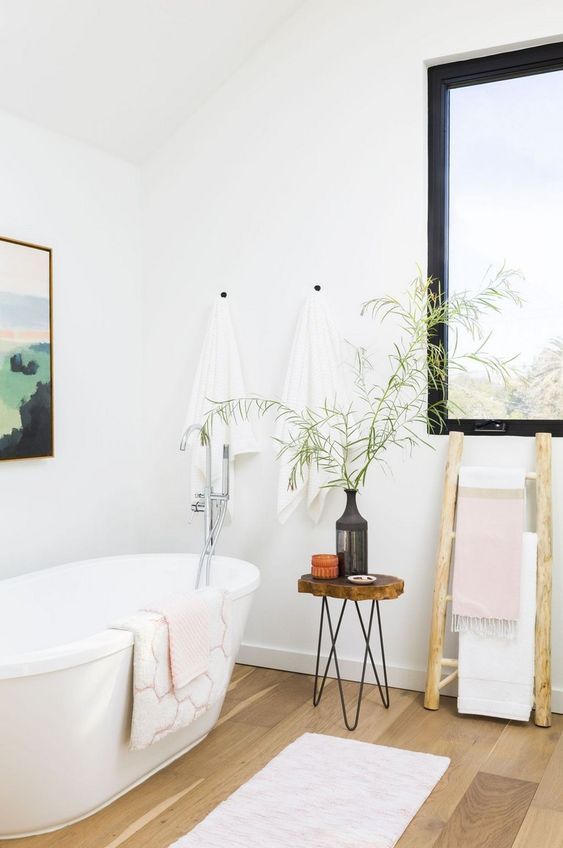 a serene Scandinavian bathroom with an oval tub, a wooden stool with hairpin legs and a blakc frame window