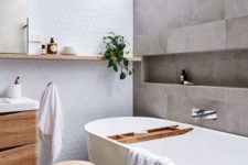 a serene Scandinavian bathroom with grey tiles, a white statement wall, much natural wood in decor and a skylight