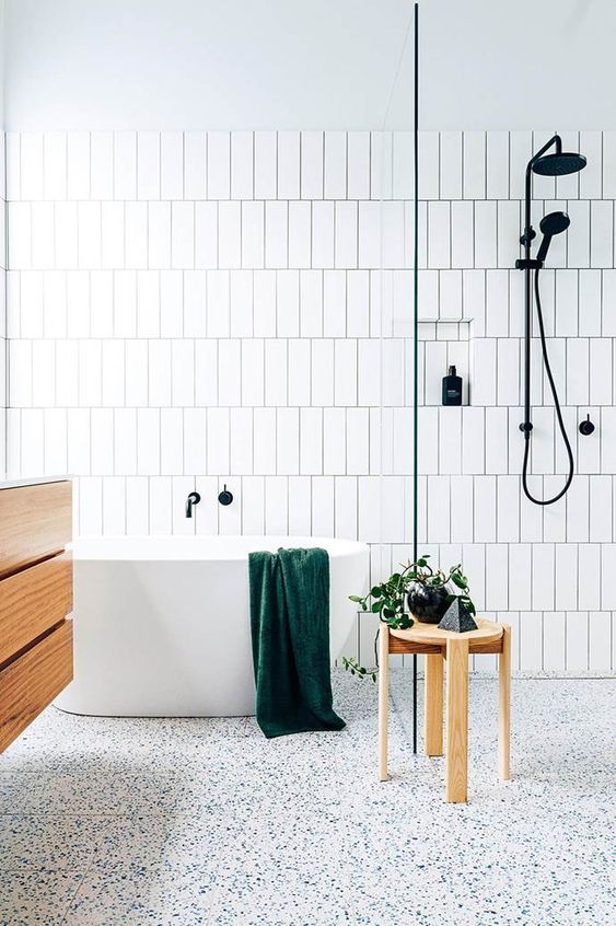 a serene Scandinavian bathroom with speckled floor, white tiles with black grout and wooden furniture
