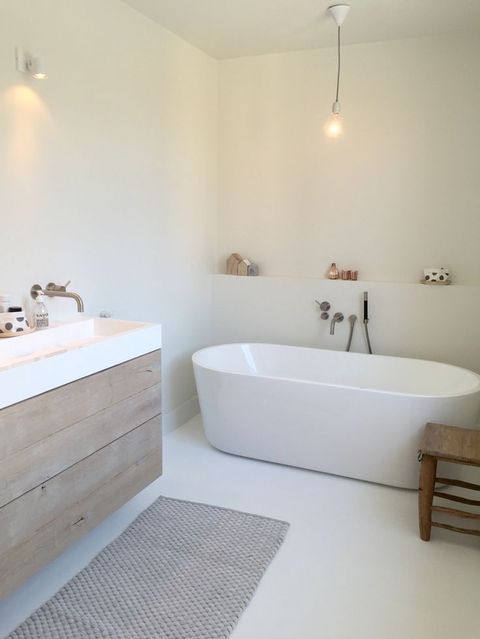a serene white Nordic bathroom with an oval bathtub, a wooden vanity and a cozy rug