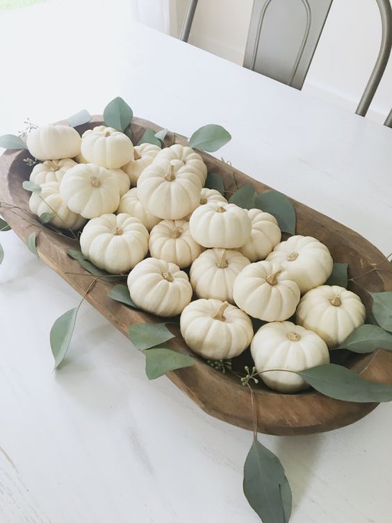 a simple and elegant fall centerpiece of a dough bowl filled with white pumpkins and some greenery