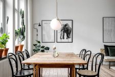 a simple and serene dining space with a stained wooden table, matching chairs, potted plants and a statement pendant lamp