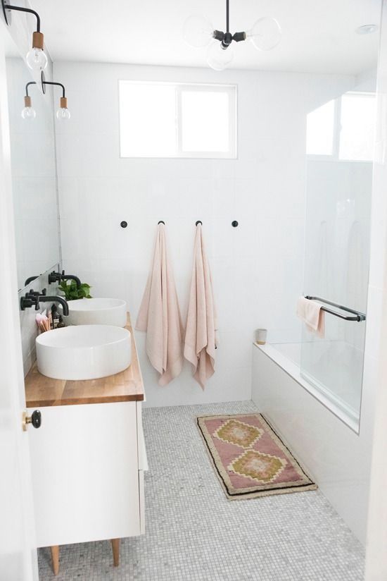 a small Scandinavian bathroom with blush towels, a pink rug, a vanity with a wooden top and sinks