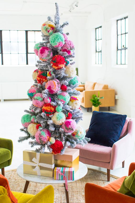 a snowy Christmas tree decorated with colorful pompoms and with colorful gifts is a very nice and bright idea