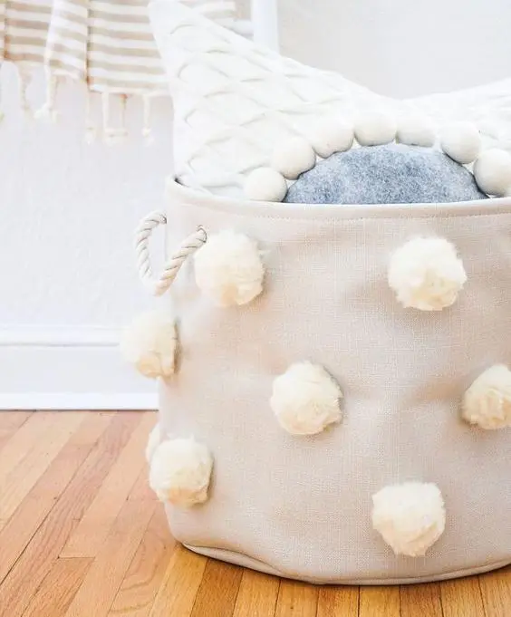 a tan fabric basket with white pompoms and white rope handles is a stylish storage piece to rock