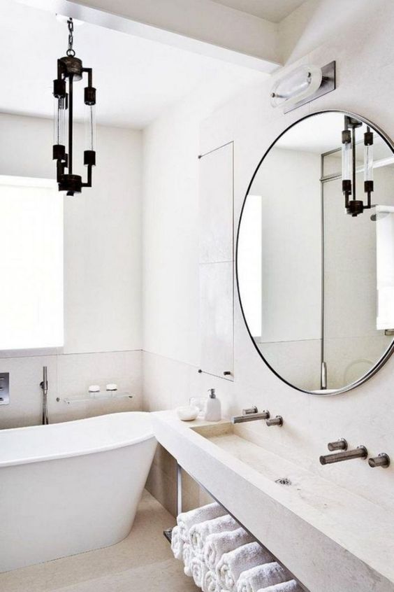 a welcoming neutral Scandinavian bathroom with much stone and concrete, a tub and a catchy chandelier