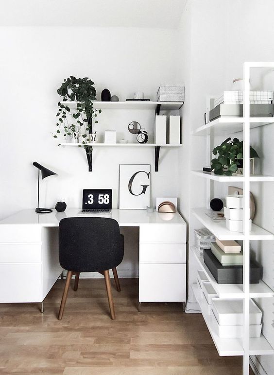 a white Scandinavian home office with a sleek desk, wall-mounted shelves, potted greenery, a comfy black chair and a table lamp