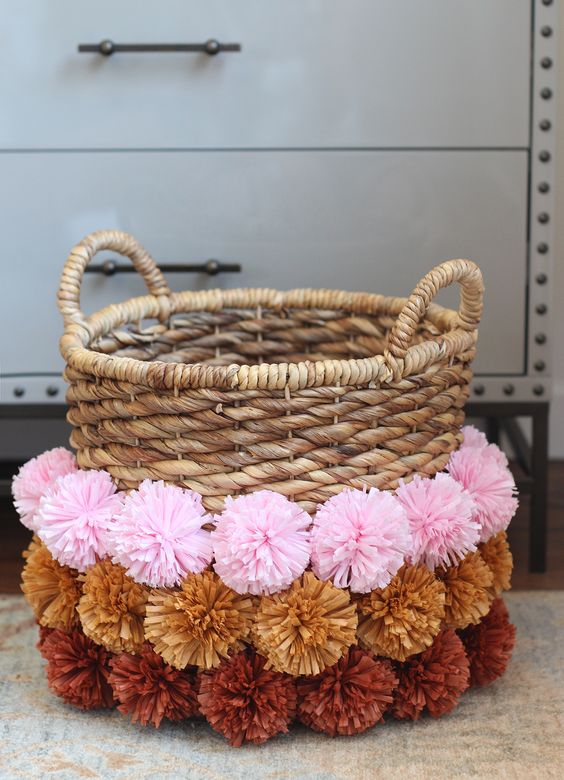 a woven basket decorated with colorful pompoms is a nice storage unit that you may use