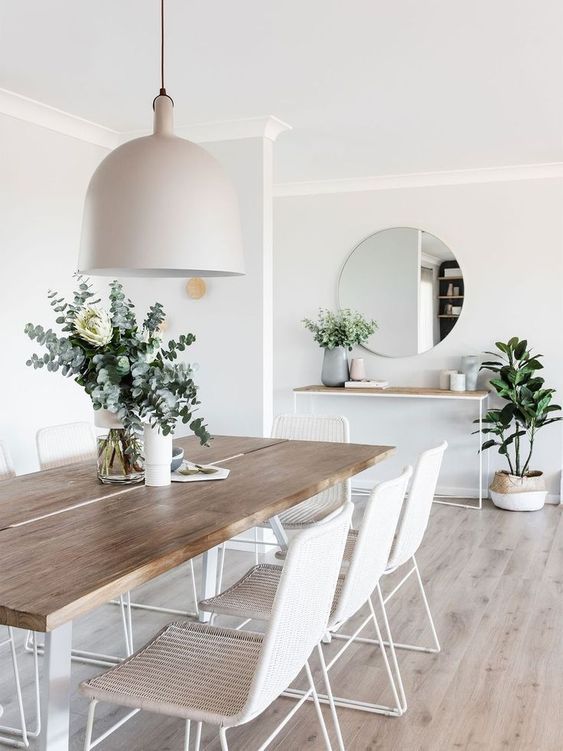 an airy Scandi dining room with a sleek stained dining table, woven chairs, a tan pendant lamp and a console table plus a round mirror