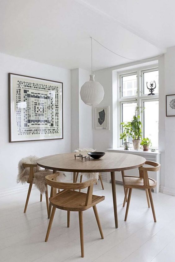 an airy Scandinavian dining nook with a round table and matching wooden chairs, a statement artwork and a pendant lamp