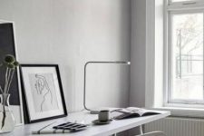 an airy Scandinavian home office with a shared desk, a white chair, black and white artworks and a table lamp