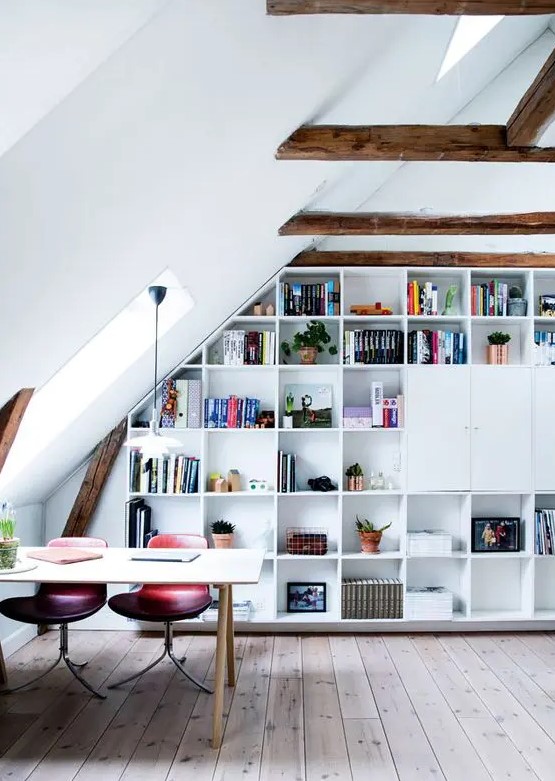 An attic home office with stained wooden beams, a built in storage unit, a desk, pink and purple chairs and some skylights to give more natural light