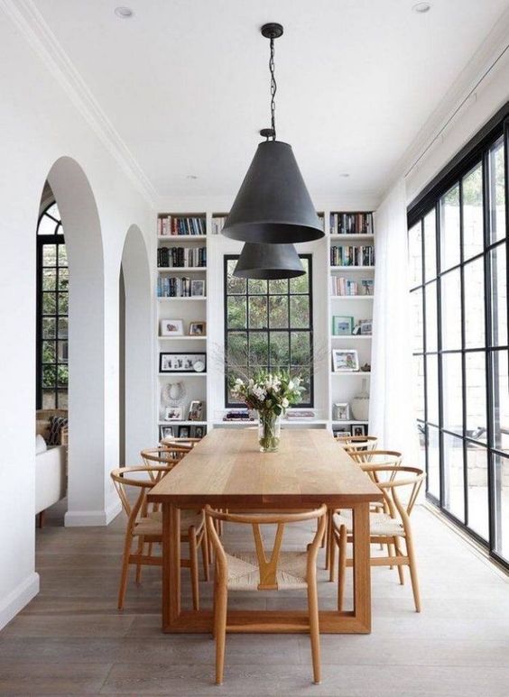 An elegant Scandinavian dining room with a stained table and chairs, built in shelves and much natural light through the windows