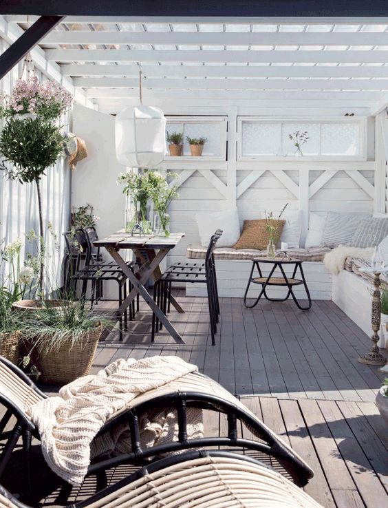 An inviting Scandinavian terrace with a dark dining set, a built in whit bench, a hairpin leg table and rattan loungers