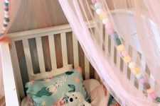 colorful pompom garlands and a light canopy to accent a baby’s crib and make it cozier and welcoming